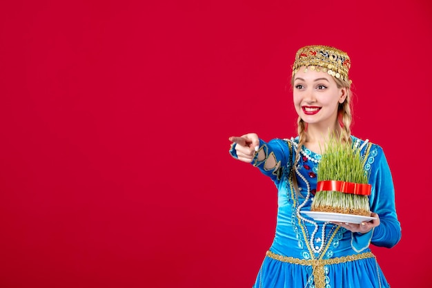 Porträt einer aserbaidschanischen frau in traditioneller kleidung mit grünem samen auf rotem hintergrund konzept novruz tänzerin frühling