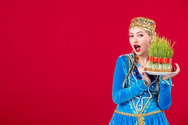 Kostenloses Foto porträt einer aserbaidschanischen frau in traditioneller kleidung mit grünem semeni auf rotem hintergrund novruz konzept ethnische tänzer frühling