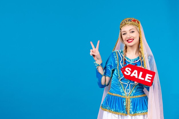 Porträt einer aserbaidschanischen Frau in traditioneller Kleidung mit Verkauf Typenschild auf blauem Hintergrund Farbe einkaufen Frühling Novruz ethnischen