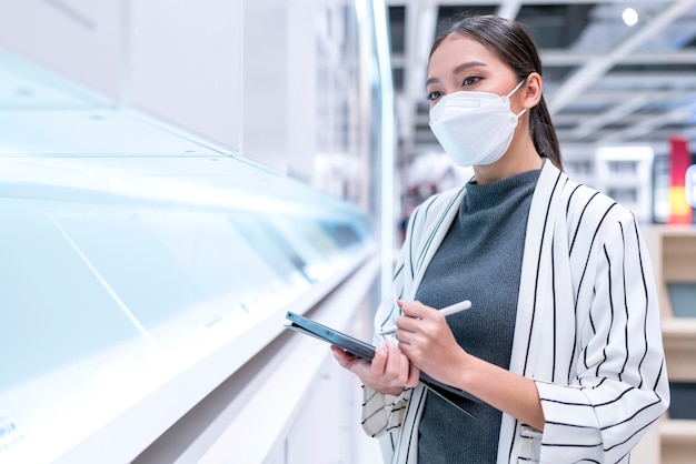 Porträt einer asiatischen geschäftsinhaberin, die eine maske verwendet, um die menge des vorrätigen produktinventars im regal des versand- und lieferservices des handelslagers zu überprüfen