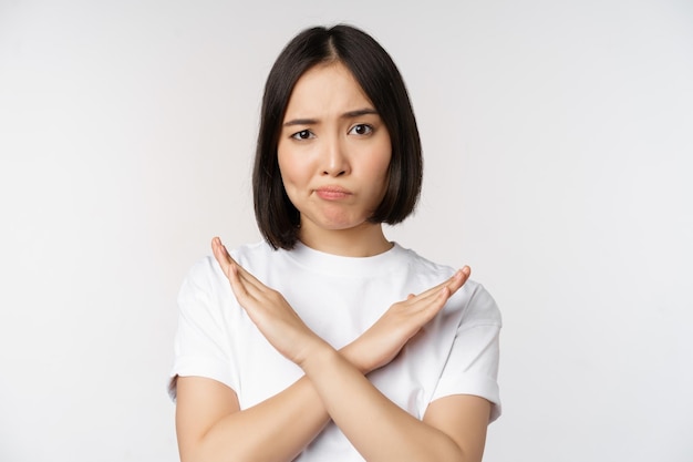 Porträt einer asiatischen Koreanerin, die eine Stoppverbotsgeste zeigt, die ein Armkreuzzeichen zeigt, das im T-Shirt auf weißem Hintergrund steht Kopierbereich
