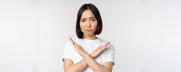 Porträt einer asiatischen Koreanerin, die eine Stoppverbotsgeste zeigt, die ein Armkreuzzeichen zeigt, das im T-Shirt auf weißem Hintergrund steht Kopierbereich