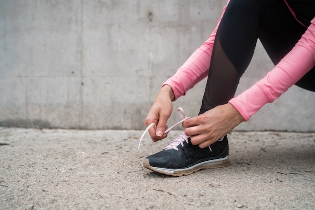 Porträt einer athletischen Frau, die ihre Schnürsenkel bindet und sich zum Joggen im Freien bereit macht. Sport und gesunder Lebensstil Konzept.