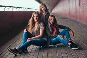 Kostenloses Foto porträt einer attraktiven familie. mutter und ihre töchter sitzen zusammen auf einem skateboard an einem brückenfußweg.