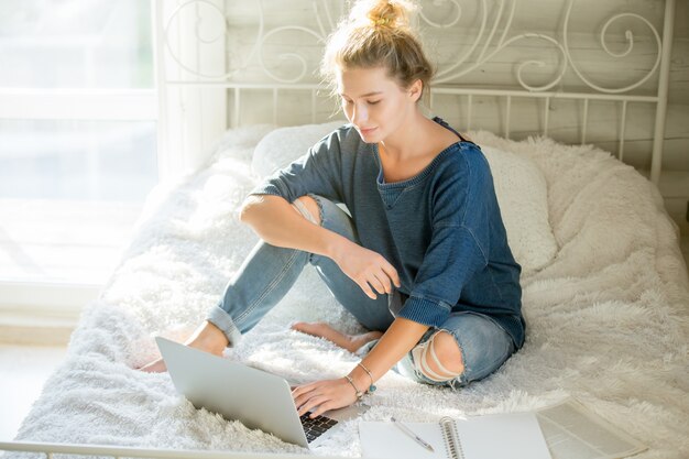 Porträt einer attraktiven Frau sitzt auf dem Bett mit Laptop