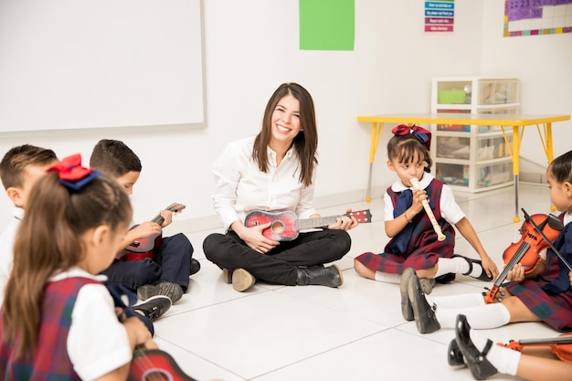 Porträt einer attraktiven hispanischen Brünette, die einer Gruppe von Vorschulkindern Musik beibringt