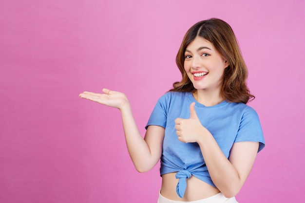 Porträt einer aufgeregten jungen Frau, die ein lässiges T-Shirt trägt, hält die Hand und demonstriert Angebotsanzeigen, die über rosafarbenem Hintergrund isoliert sind