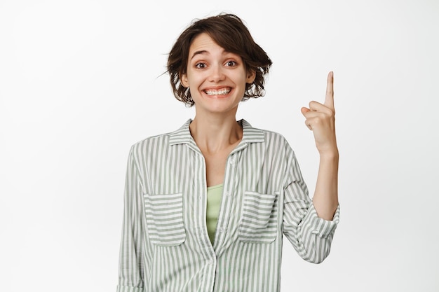 Porträt einer aufgeregten lächelnden Frau, die mit dem Finger nach oben zeigt und glücklich aussieht, Werbung demonstriert, auf den Link klickt und vor weißem Hintergrund steht