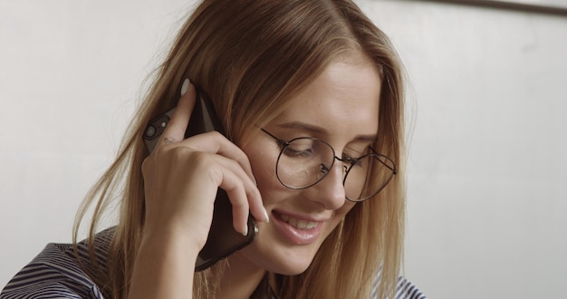 Porträt einer blonden Frau, die auf einem mobilen Smartphone im Bürostil spricht