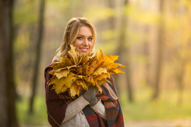 Porträt einer blonden Frau, die mit einem Blumenstrauß aus Ahornblättern steht. Schöne Dame, die toothy lächelt und in die Kamera schaut