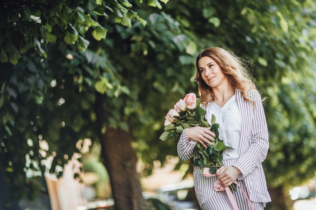 Porträt einer blonden Frau mittleren Alters in Freizeitkleidung auf der Straße mit einem Strauß Rosen