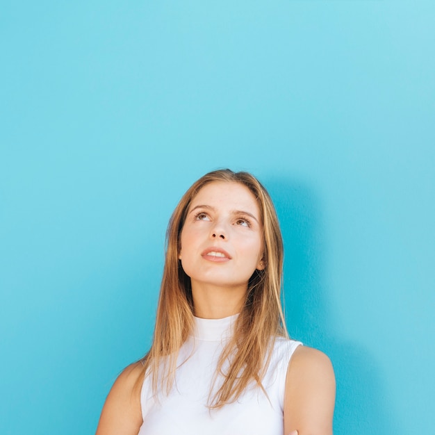 Porträt einer blonden jungen Frau, die oben gegen blauen Hintergrund schaut