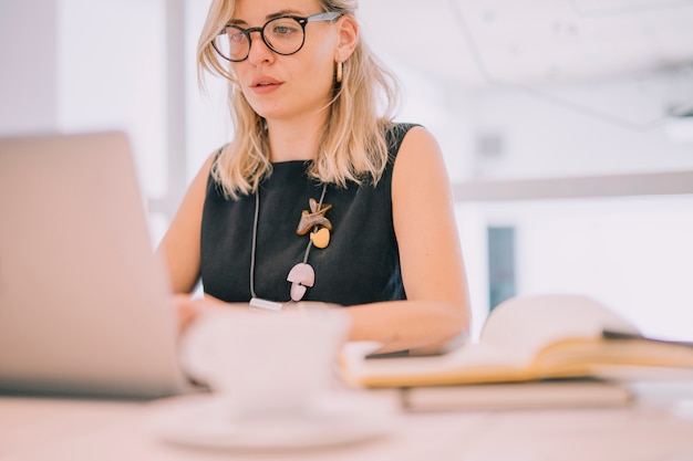 Kostenloses Foto porträt einer blonden jungen geschäftsfrau, die laptop im büro betrachtet