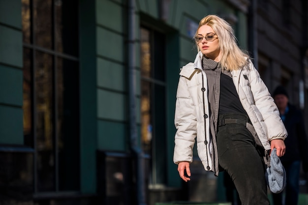 Porträt einer blonden modernen jungen Frau, die vor Gebäude steht