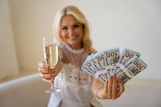 Porträt einer blonden reichen Frau mittleren Alters mit Sektglas und Banknoten