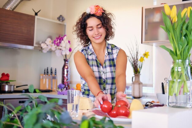 Porträt einer brünetten attraktiven Frau mit lockigem Haar in einer Wohnküche mit vielen Blumen.