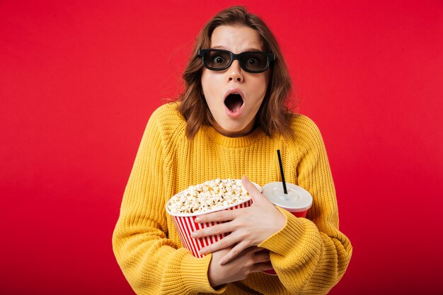 Porträt einer entsetzten Frau in der Sonnenbrille, die Popcorn hält