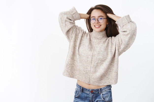 Porträt einer entspannten, zarten, attraktiven Frau mit Brille und warmem, stylischem Pullover, die Haare massiert und sich freudig streckt