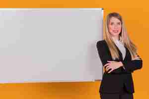 Kostenloses Foto porträt einer erfolgreichen jungen geschäftsfrau, die nahe dem whiteboard gegen einen orange hintergrund steht