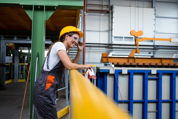 Porträt einer Fabrikarbeiterin, die sich auf Metallgeländer in der industriellen Produktionshalle stützt