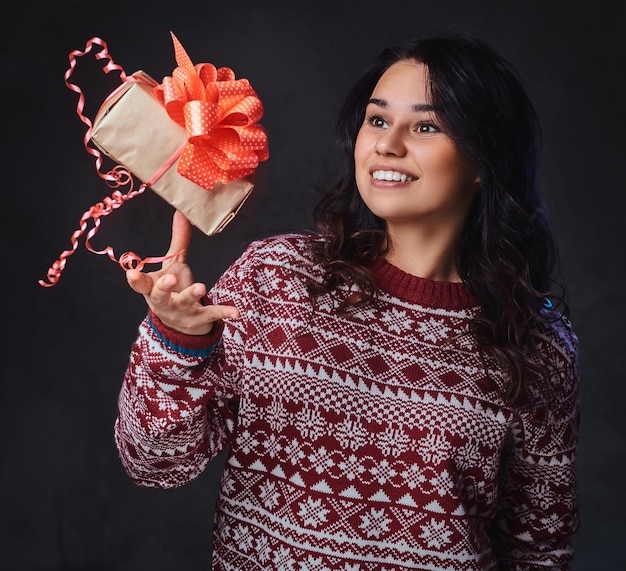 Porträt einer festlich lächelnden brünetten Frau mit langen lockigen Haaren, gekleidet in einen roten Pullover, hält Weihnachtsgeschenke.