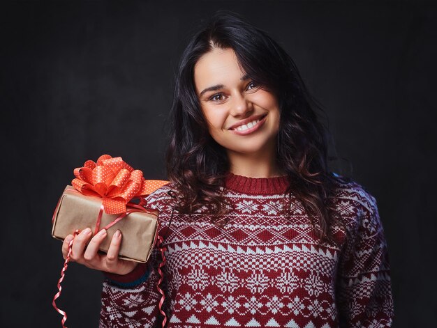 Porträt einer festlich lächelnden brünetten Frau mit langen lockigen Haaren, gekleidet in einen roten Pullover, hält Weihnachtsgeschenke.