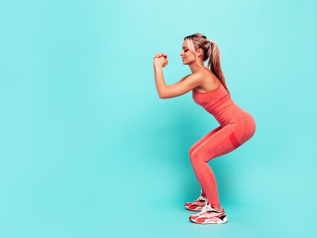Porträt einer Fitness-Frau in rosafarbener Sportkleidung Junges schönes Modell mit perfektem KörperFrau posiert in der Nähe der Wand im StudioFröhlich und glücklich Stretching vor dem Training