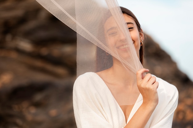 Kostenloses Foto porträt einer frau am strand, die ihr gesicht hinter einem schleier versteckt