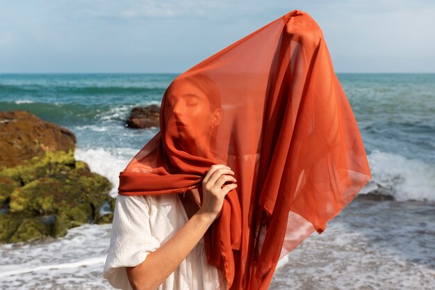 Porträt einer Frau am Strand, die ihr Gesicht mit einem Schleier bedeckt