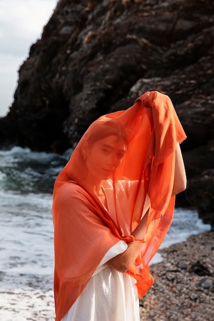 Porträt einer Frau am Strand, die ihr Gesicht mit einem Schleier bedeckt