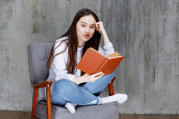 Porträt einer Frau, die ein Buch liest, während sie auf einem Sessel sitzt. Foto in hoher Qualität