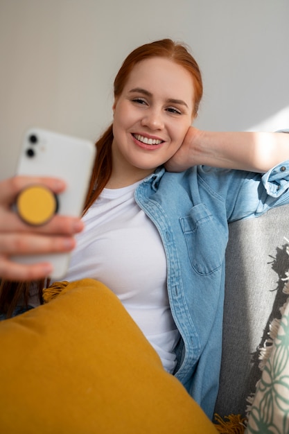 Porträt einer Frau, die ihr Smartphone zu Hause auf der Couch benutzt, indem sie sie an der Pop-Buchse hält