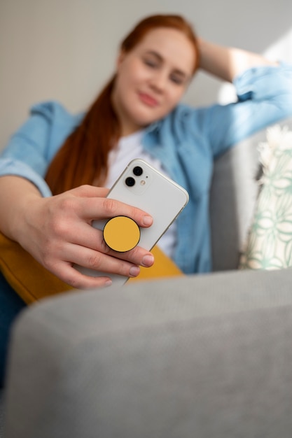 Porträt einer Frau, die ihr Smartphone zu Hause auf der Couch benutzt, indem sie sie an der Pop-Buchse hält