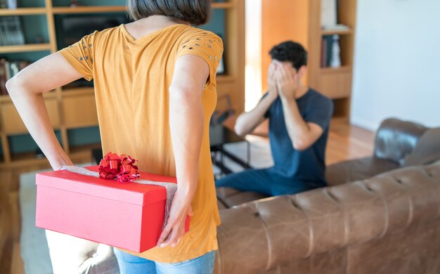 Porträt einer Frau, die ihren Freund mit einem Geschenk überrascht. Feier und Valentinstag Konzept.