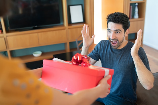 Porträt einer Frau, die ihren Freund mit einem Geschenk überrascht. Feier und Valentinstag Konzept.