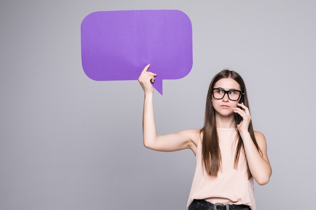 Porträt einer Frau, die leere Sprechblase hält und auf Handy lokalisiert über graue Wand spricht