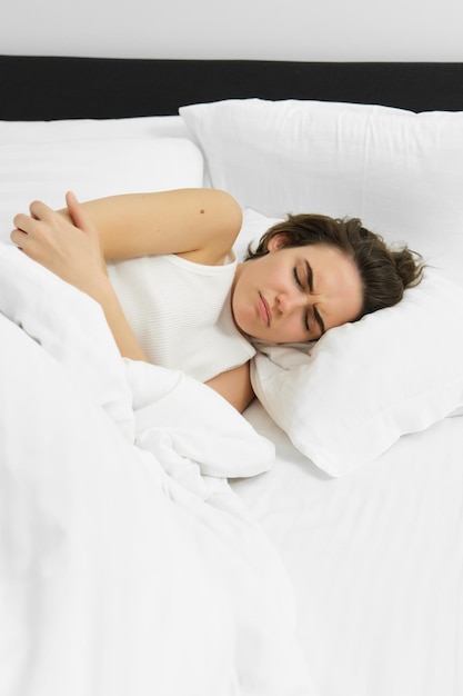 Porträt einer Frau, die mit Magenschmerzen im Bett liegt, Menstruationskrämpfe hat, die Stirn runzelt und Schmerzen fühlt