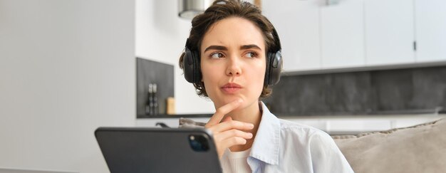 Kostenloses Foto porträt einer frau, die musik in kopfhörern hört und denkt, während sie auf einem digitalen tablet arbeitet