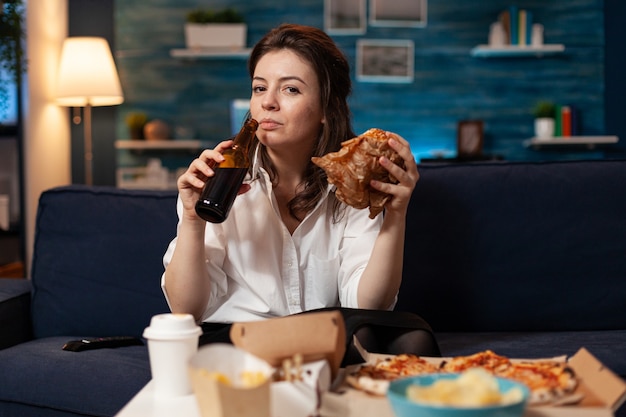 Porträt einer Frau, die während der Fastfood-Mittagessenbestellung in die Kamera schaut, die sich auf dem Sofa entspannt