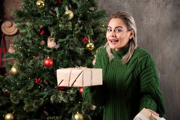 Porträt einer Frau gekleidet im grünen Pullover, der Stapel von Geschenkboxen hält und Kamera betrachtet