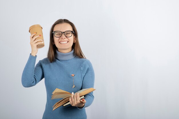 Porträt einer Frau mit Brille, die ein Buch und eine Tasse Kaffee hält.