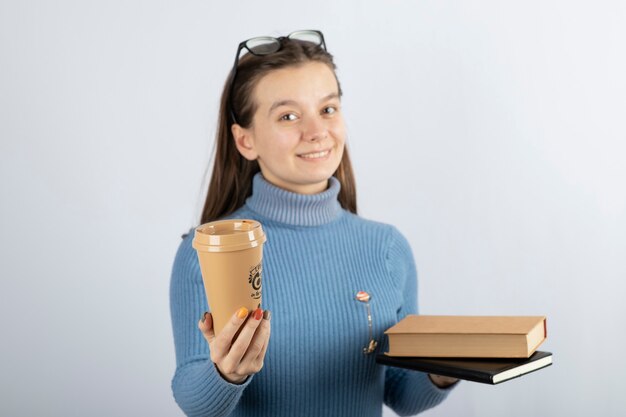 Porträt einer Frau mit Brille, die zwei Bücher und eine Tasse Kaffee hält.