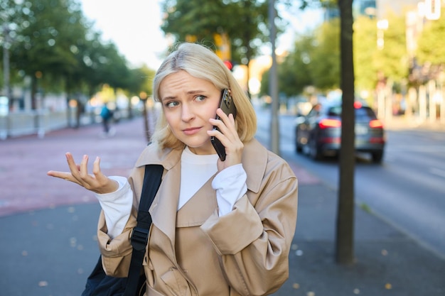 Kostenloses Foto porträt einer frau mit einem verwirrten gesicht, die am mobiltelefon spricht und auf der straße steht, um einen anruf zu beantworten