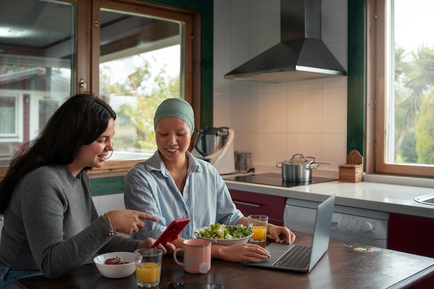 Porträt einer Frau mit Krebs, die mit einem Freund zu Hause einen Laptop benutzt