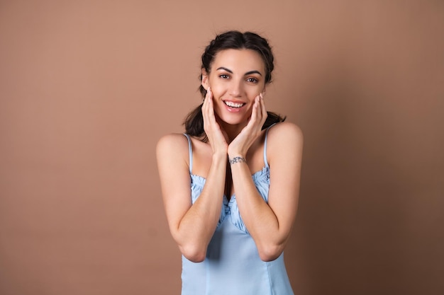 Porträt einer Frau mit perfekter Haut und natürlichem Make-up auf beigem Hintergrund mit Zöpfen, fröhlich und gut gelaunt in einem blauen Frühlingssommerkleid