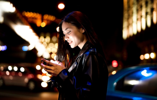 Porträt einer Frau mit Smartphone nachts in den Lichtern der Stadt city