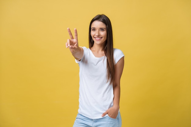 Porträt einer fröhlichen jungen Frau, die zwei Finger oder eine Siegesgeste auf gelbem Hintergrund zeigt