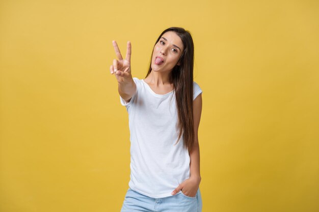 Porträt einer fröhlichen jungen Frau, die zwei Finger oder eine Siegesgeste auf gelbem Hintergrund zeigt