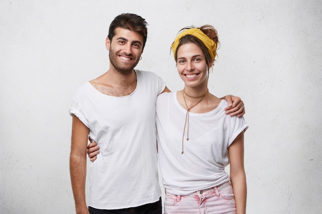 Porträt einer fröhlichen jungen Frau und eines Mannes in weißen T-Shirts, die sich umarmen, breit schauen und lächeln.