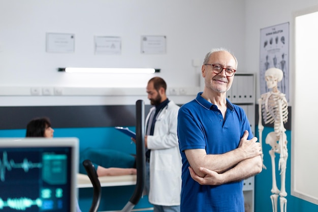 Porträt einer gealterten Person in der Klinik für körperliche Erholung zur Rehabilitation. Alter Patient mit Verletzung, der sich vorbereitet, sich mit Übung und Fitness zu erholen. Mann, der mit verschränkten Armen in die Kamera schaut